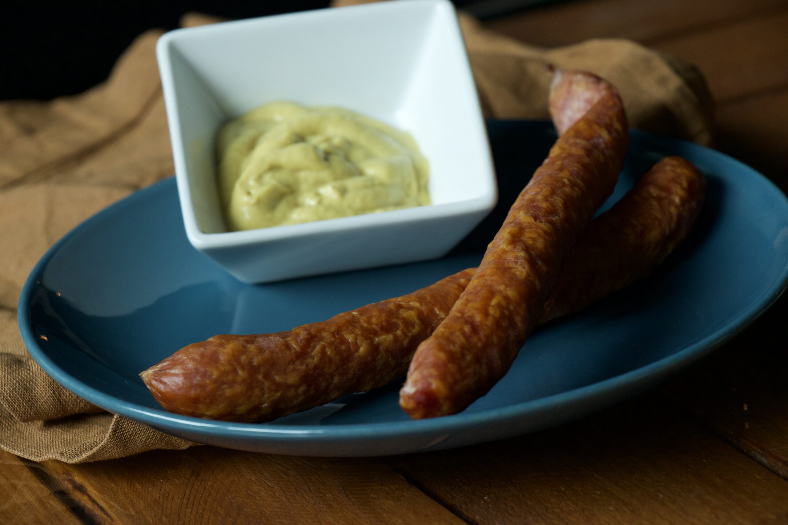 zwei PfefferbeiĂźer auf einem blauen Teller, daneben eine Schale mit Senf